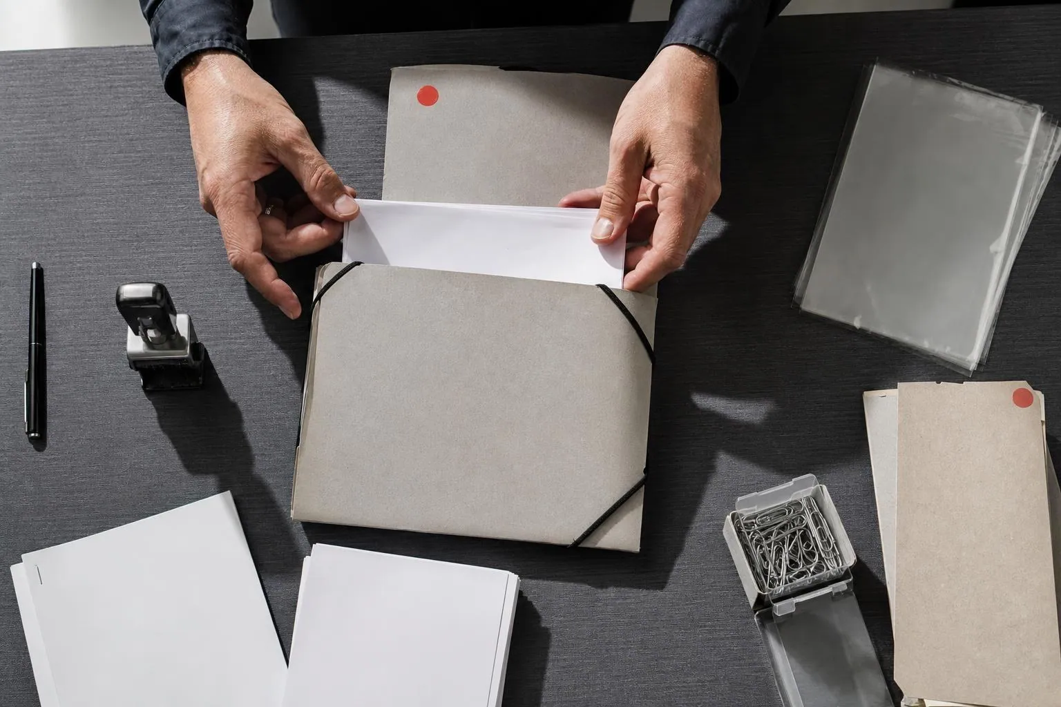 Pochette a elastiques ouverte sur un plan de travail, pieces d’un dossier etalees et rangees a la main