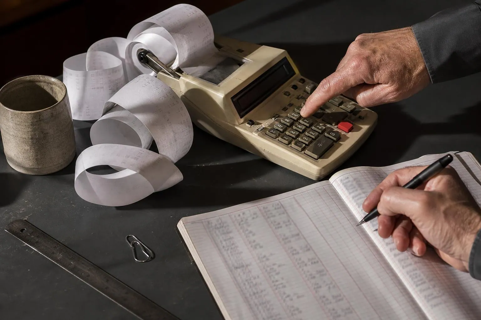 Calculatrice de bureau a bande papier en cours d’utilisation a cote d’un cahier a colonnes