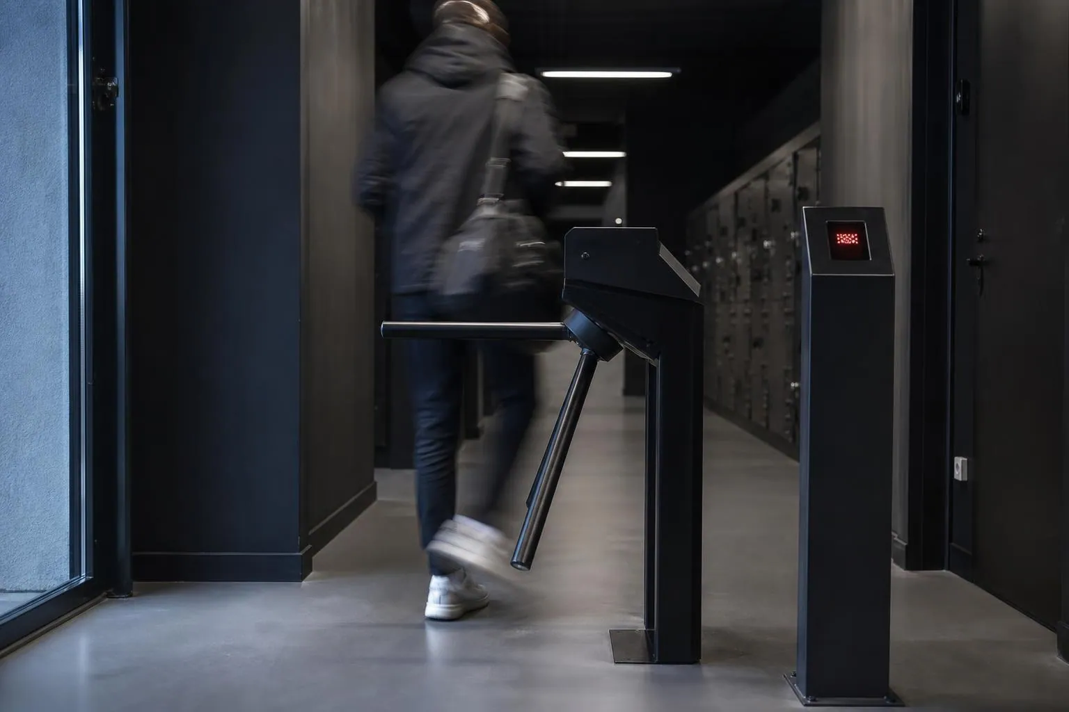 Portillon tripode metallique a l’entree d’une salle de sport, silhouette d’un adherent en mouvement