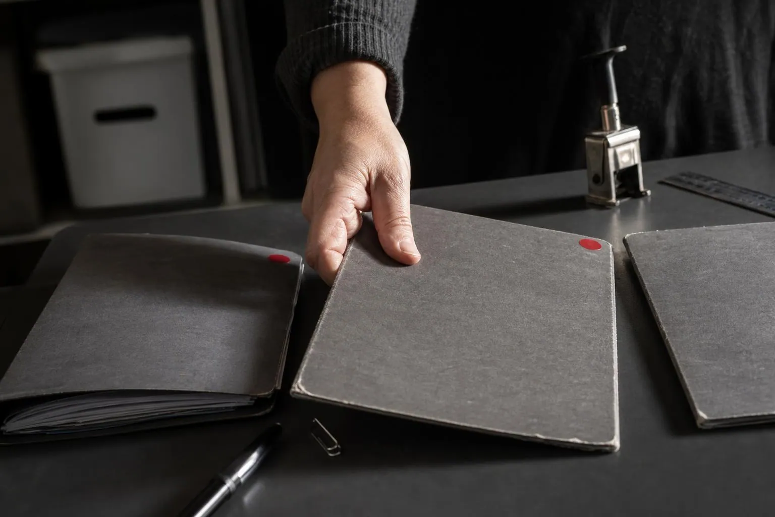 Trois chemises cartonnees alignees sur une table de bureau, une main en deplace une